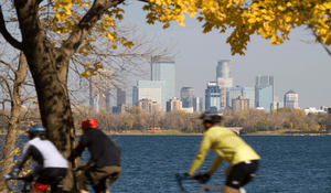 three bikers riding in front of a body of water with a city on the other side.