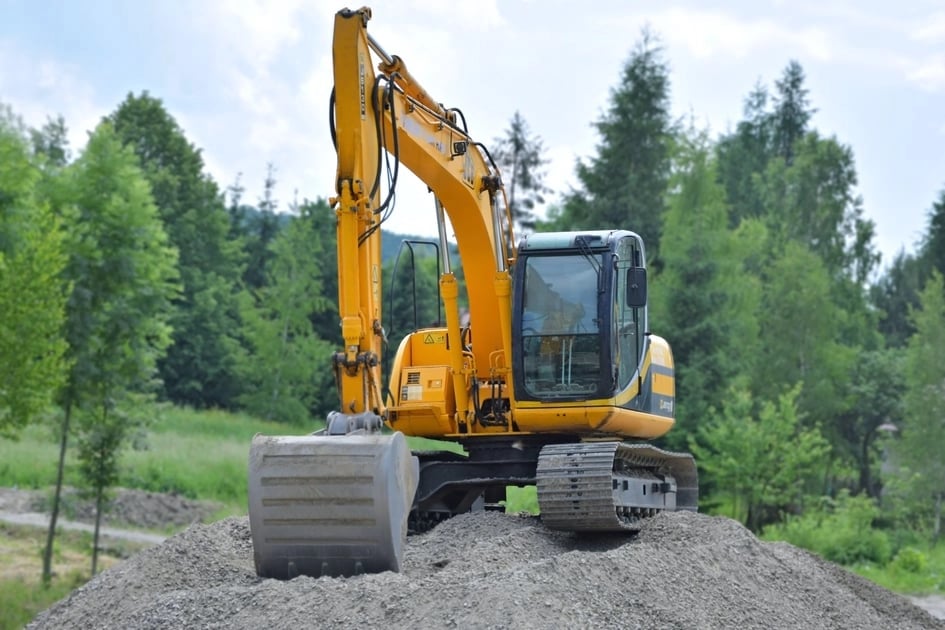 An excavator on top of a hill of gravel.