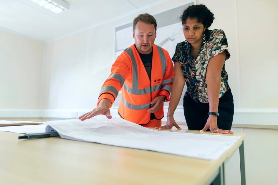 Man in safety vest explaining construction blueprints to a woman.
